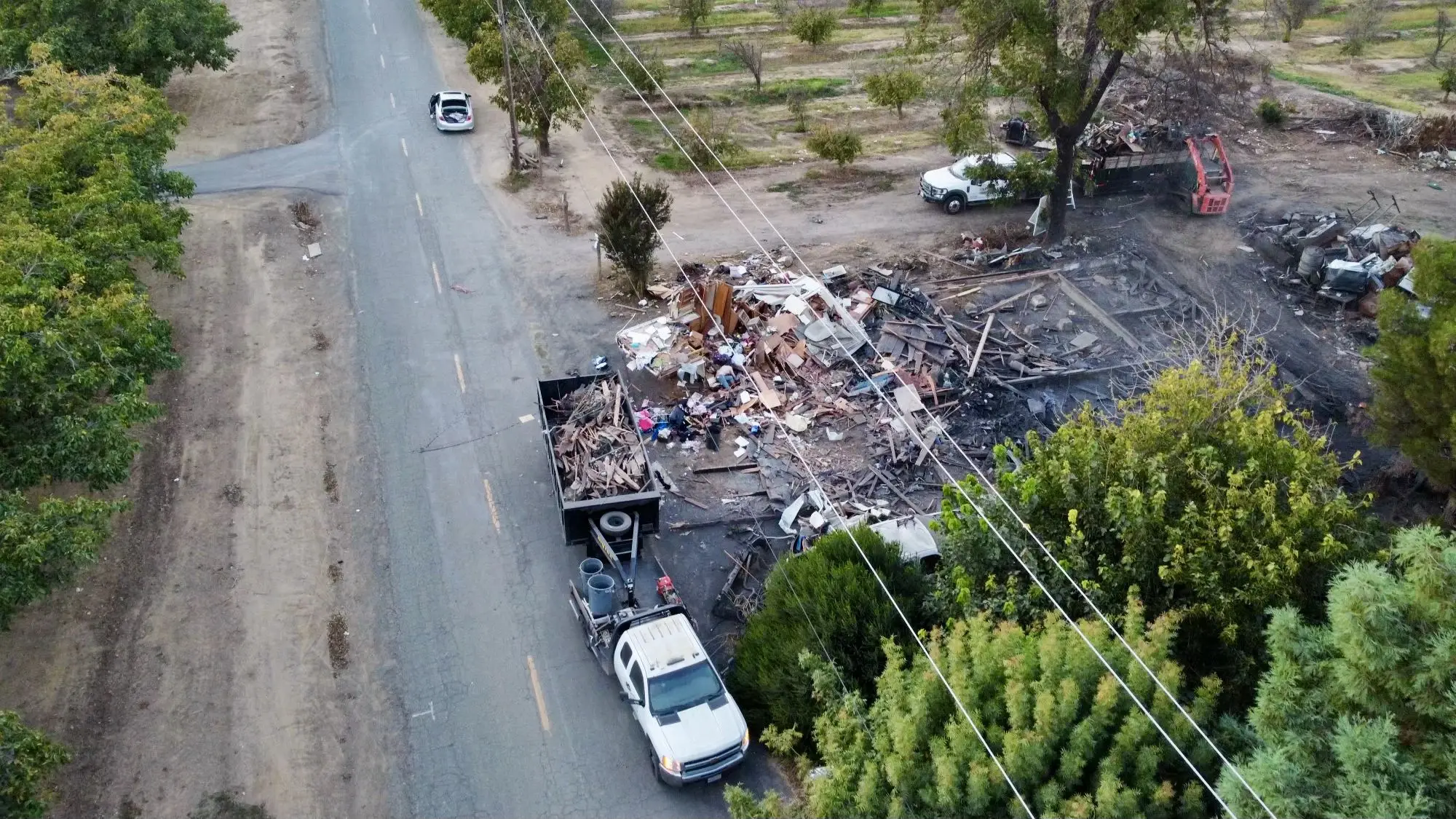 Aerial view of fire debris loaded into trucks beside a rural road