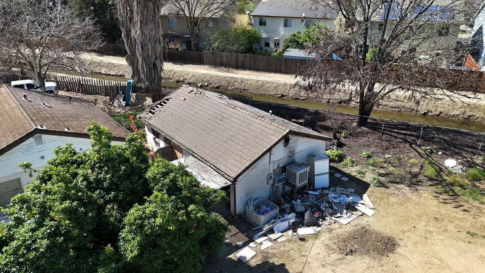 Aerial view of a detached garage with an aging roof before demolition, old appliances and scrap piled against the side wall