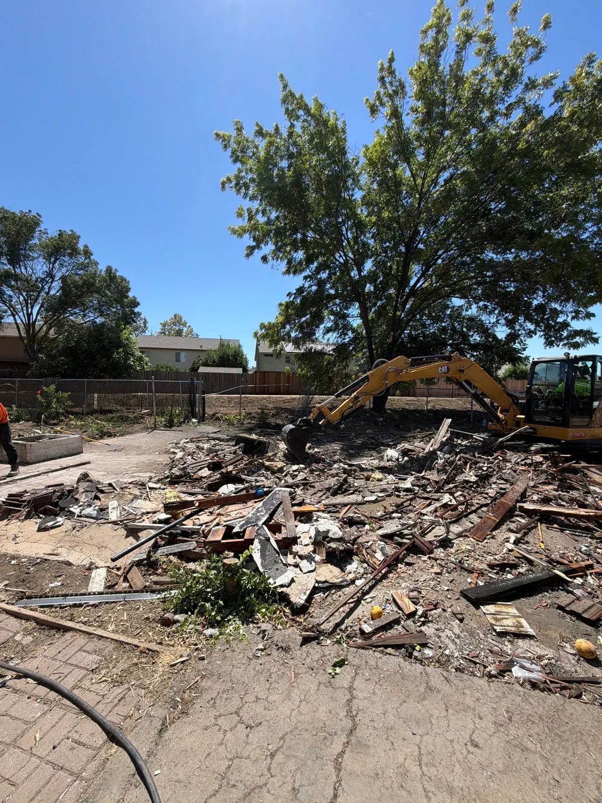 Demo Patrol excavator working a pile of wood framing, roofing, and broken concrete where the garage stood