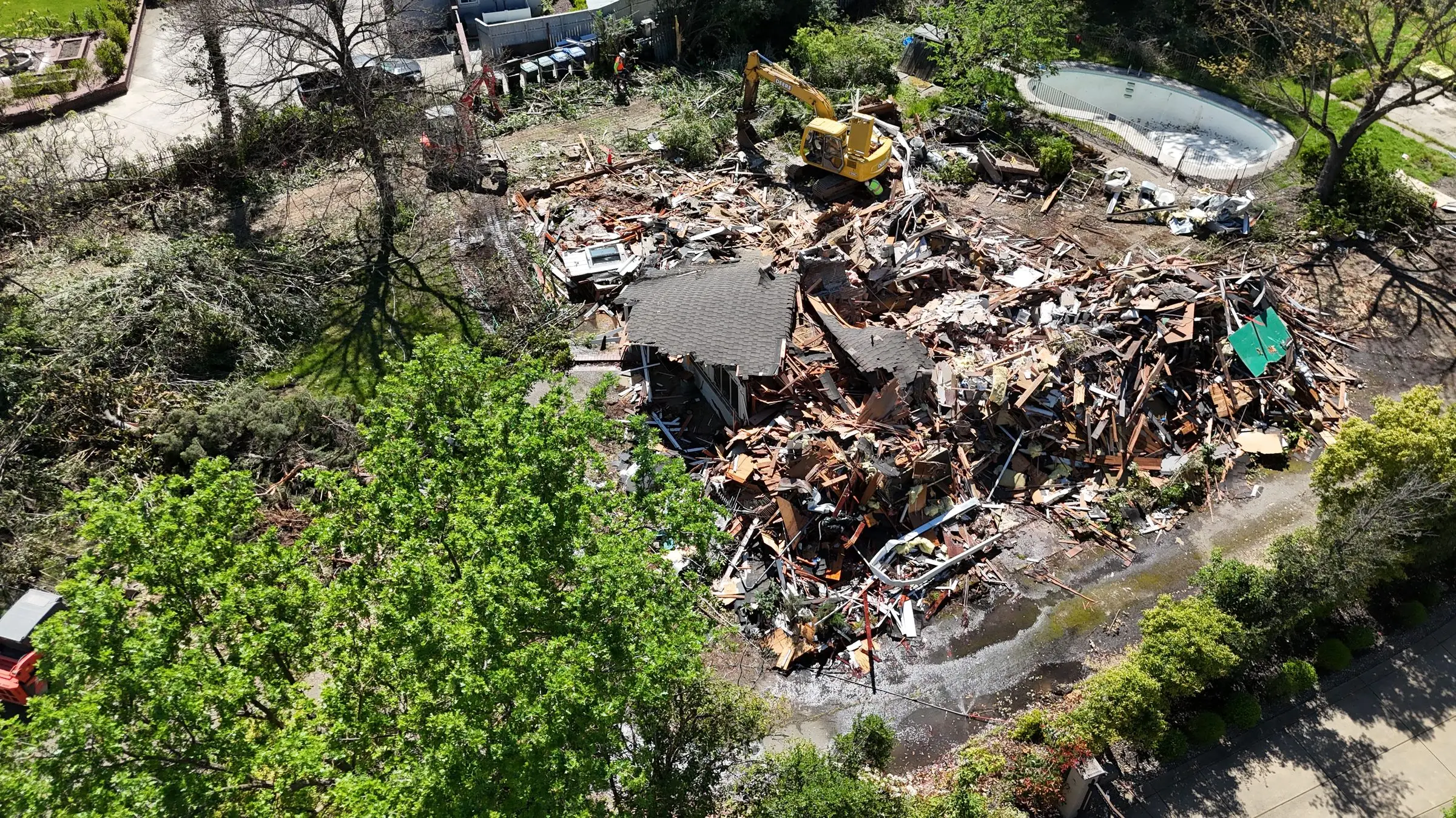 Aerial view of a house demolition debris pile next to a backyard pool