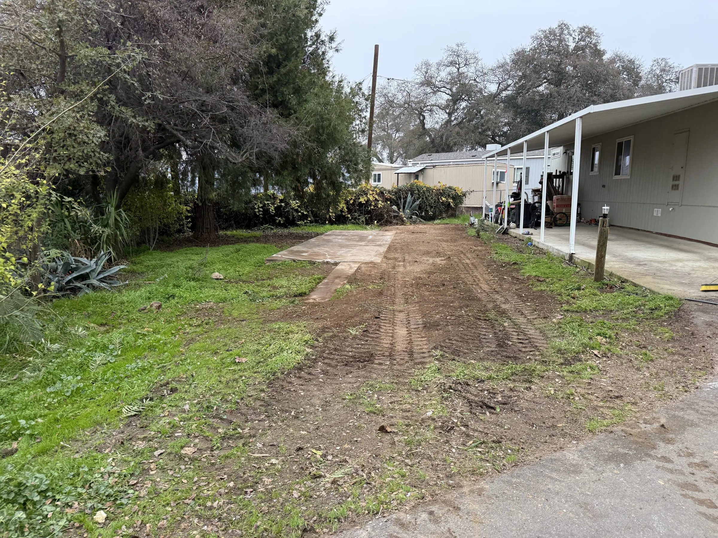 Cleared mobile home pad with concrete runners and neighboring carport