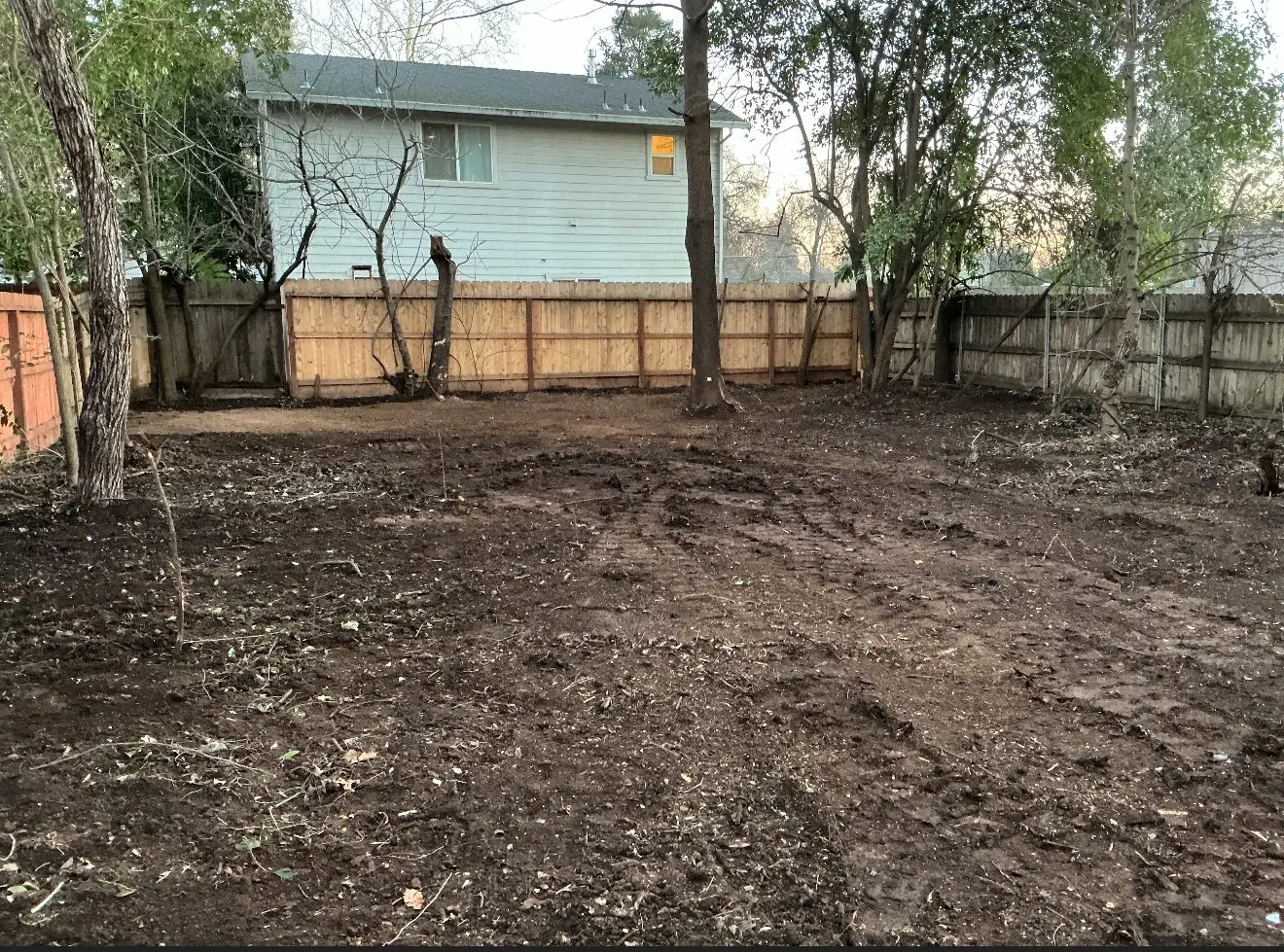 Raked and rough-graded dirt lot between wood fences