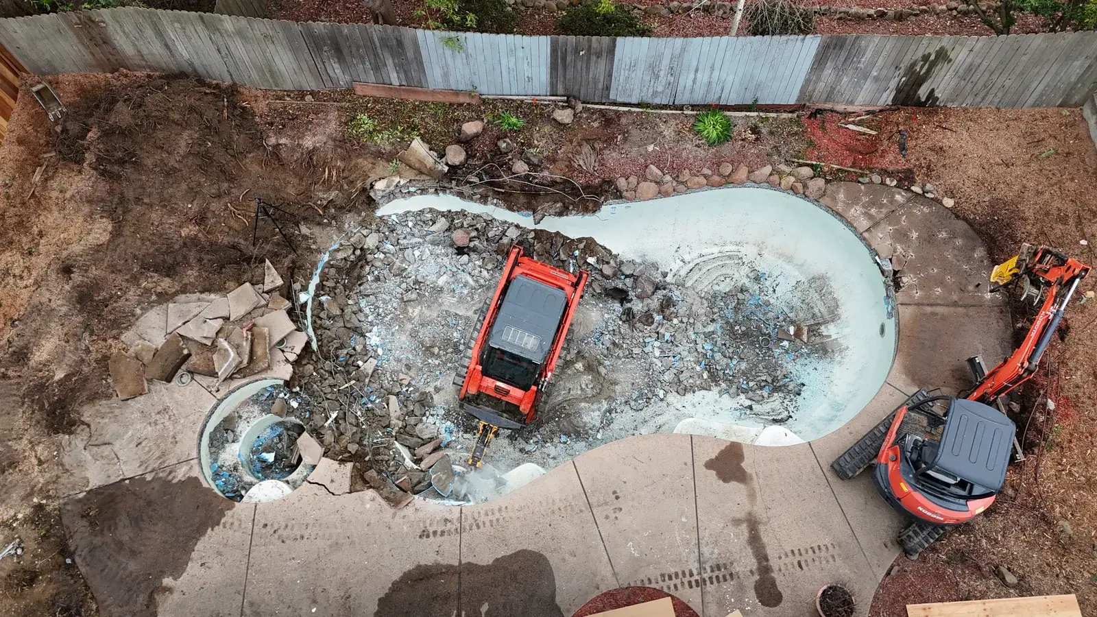 Aerial view of backyard pool demolition in Sacramento with Kubota excavator breaking out concrete shell